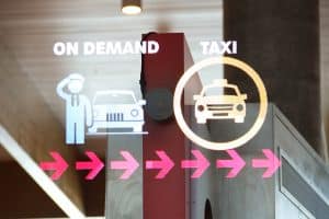 A sign with icons indicating on-demand and taxi services, reminiscent of visuals at the ACI World Technology Innovation Awards. Arrows point right: a person saluting by a car for On Demand and a car with a taxi sign for Taxi.