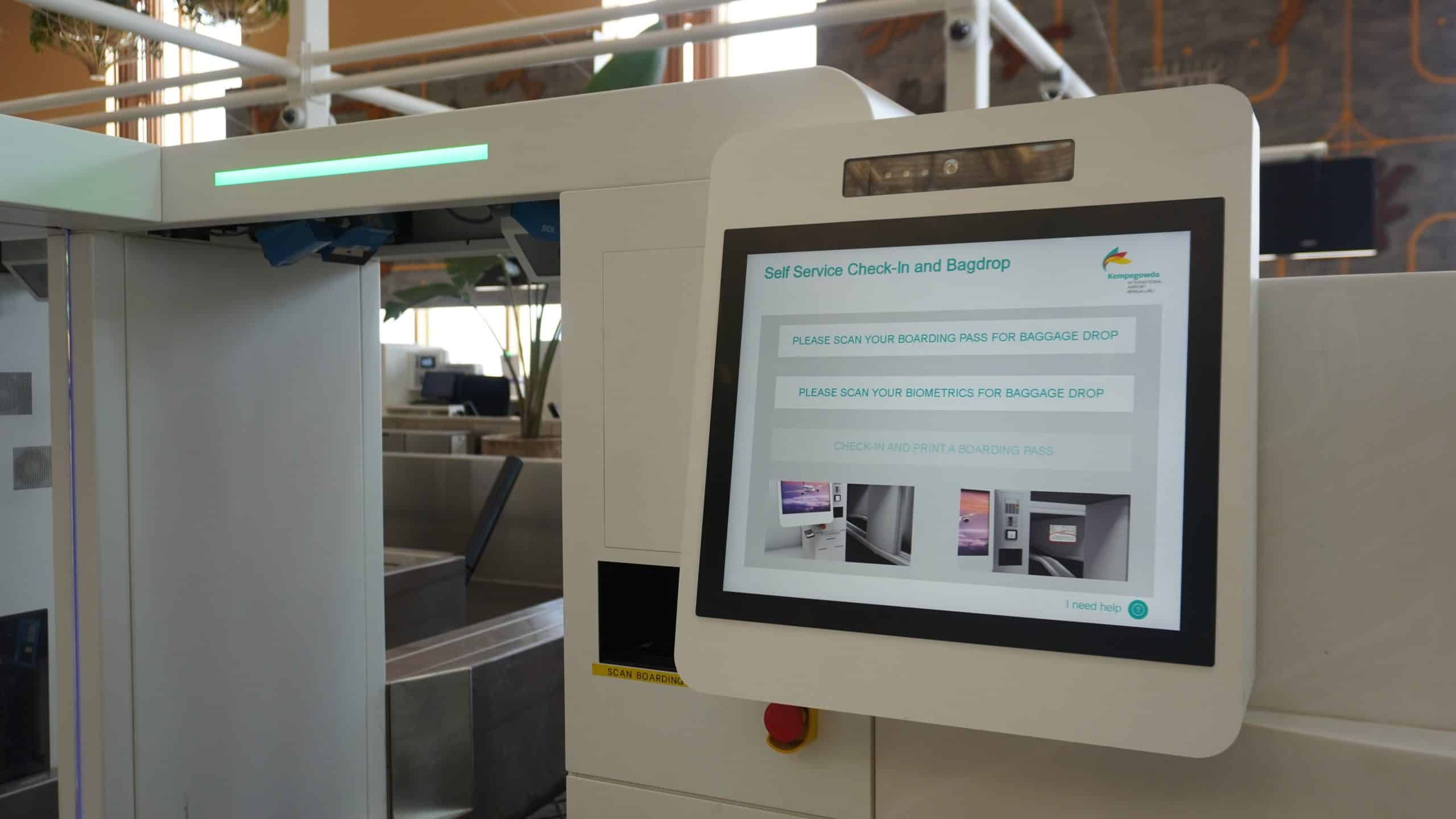A close-up of an airport self-service kiosk screen displaying instructions for check-in and bag drop, with a baggage conveyor belt visible beside it—a scene showcasing advancements recognized by the ACI World Technology Innovation Awards.