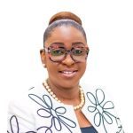 A woman with neatly tied hair and glasses, wearing a pearl necklace and a white jacket with black floral patterns, smiles at the camera against a plain white background, representing the distinguished AMPAP alumni group.